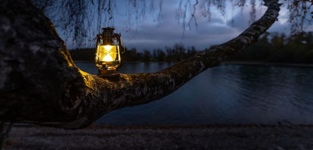 Leuchtende Laterne auf Baumstamm in der Nacht vor einem See.